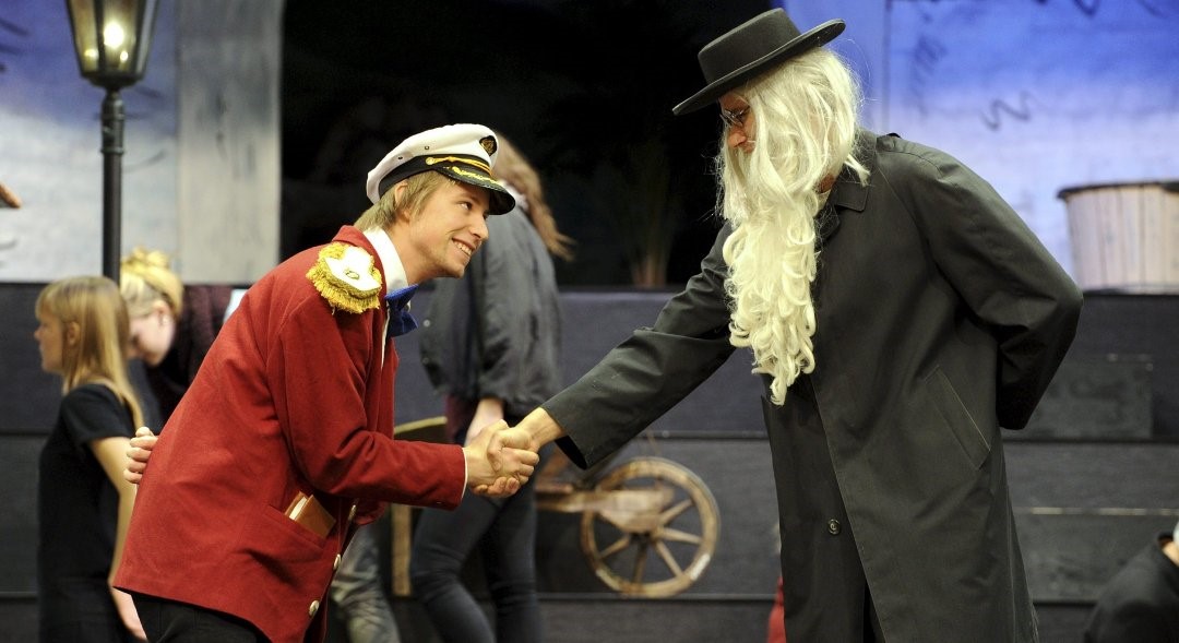 To unge menn i kostyme spiller teater og håndhilser.