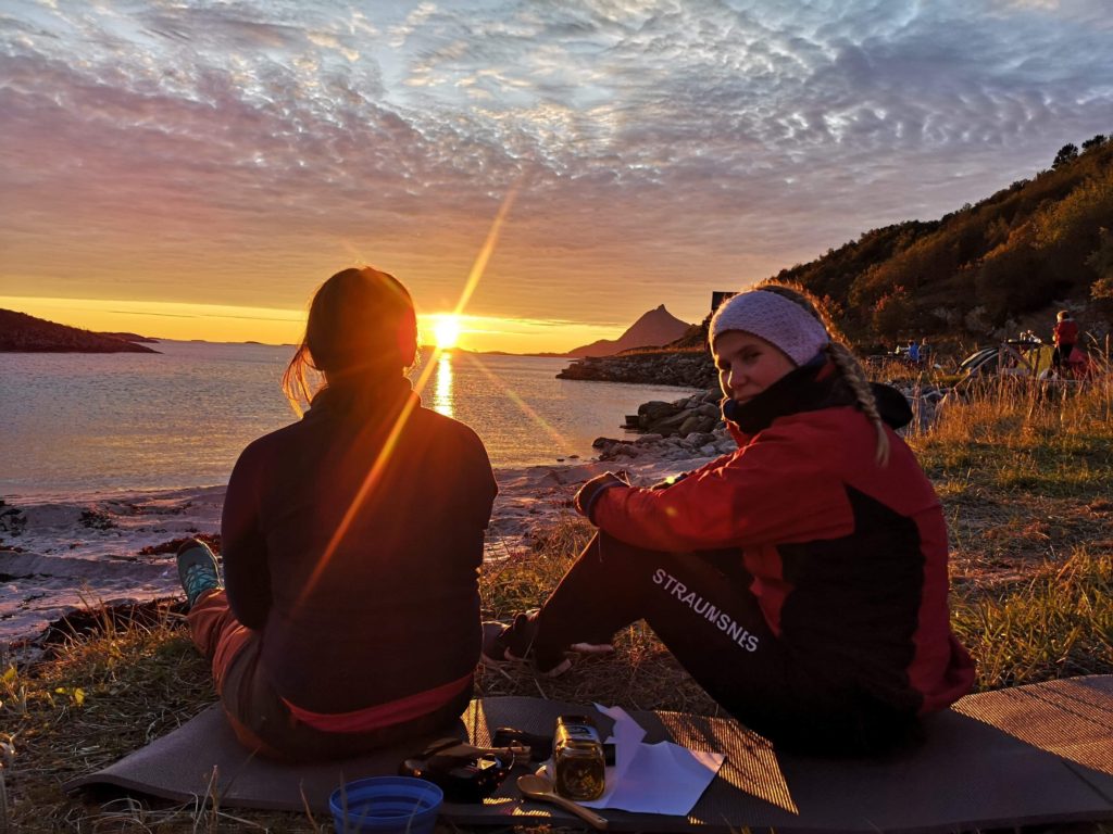solnedgang, to personer sittende i fjæra