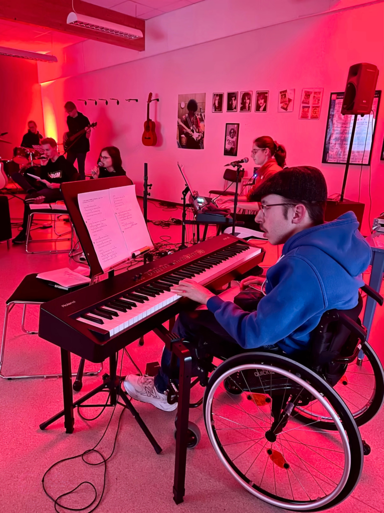 Bildet av en gutt i rullestol som spiller keyboard sammen med andre musikere. Foto over og i topp-banneret: Lundheim folkehøgskole